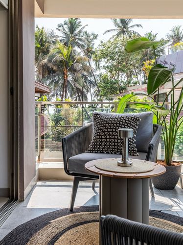 Balcony with rope-weave armchairs, patterned cushion and round side table facing palm trees