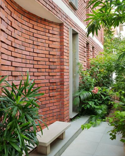 Curved textured brick facade with recessed door, stone bench, and lush garden path in Jaipur