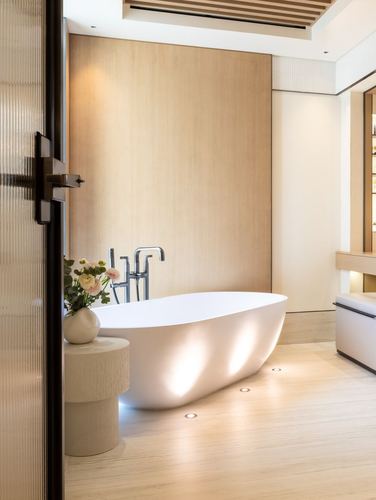 Freestanding oval tub against wood-panelled wall, backlit by recessed floor lights, in a minimalist bathroom