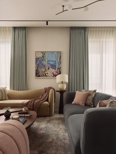 Living room with mustard and charcoal curved sofas facing a colorful framed artwork between sage curtains