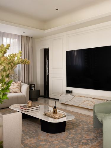 Living room with panelled wall, wall-mounted TV, marble console, and patterned rug