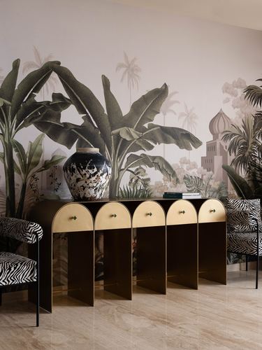 Dark and gold arched console table with zebra print chairs against a tropical mural, ceramic vase on top