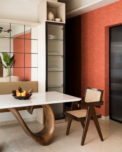 Dining nook with marble-top table on carved wood base, cane chair, and terracotta textured wall