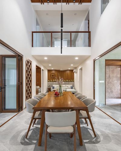 Double-height dining room with wooden table, grey chairs, and mezzanine landing above