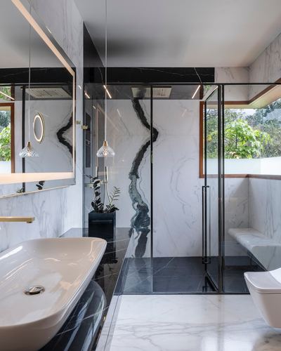 Marble bathroom with glass shower, black stone floor, brass pendant lights and vessel sink