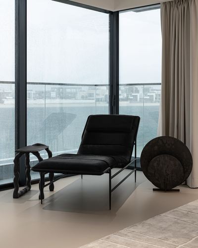 Black chaise lounge and sculptural side table by floor-to-ceiling windows overlooking Palm Jumeirah