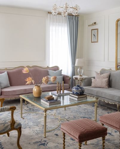 Living room with pink and grey velvet sofas around a glass coffee table under a crystal chandelier