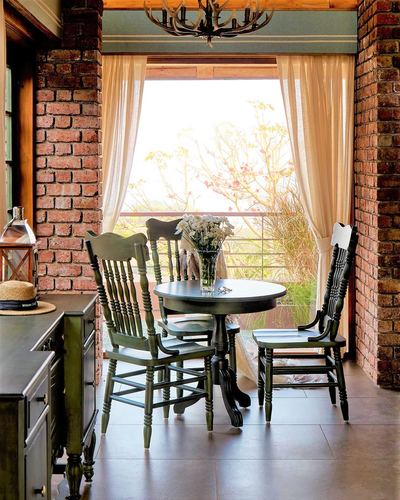Rustic dining nook with green chairs, round table, brick walls, and a window view of hills