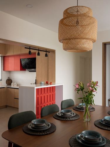 Dining table with woven pendant light and view into red-and-wood kitchen beyond