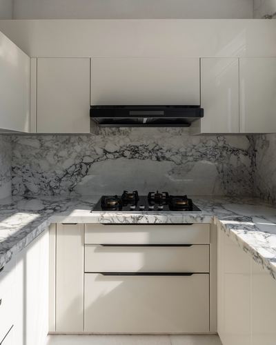White gloss kitchen corner with veined stone countertop, backsplash, and black gas hob