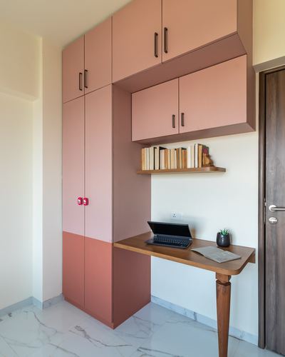 Pink and terracotta wardrobe unit with a wall-mounted desk holding a laptop and books on a shelf above