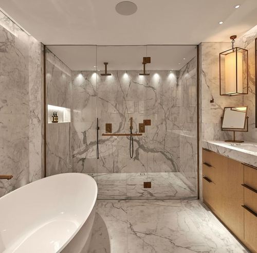Marble bathroom with freestanding tub, glass shower, brass fixtures, and wood vanity