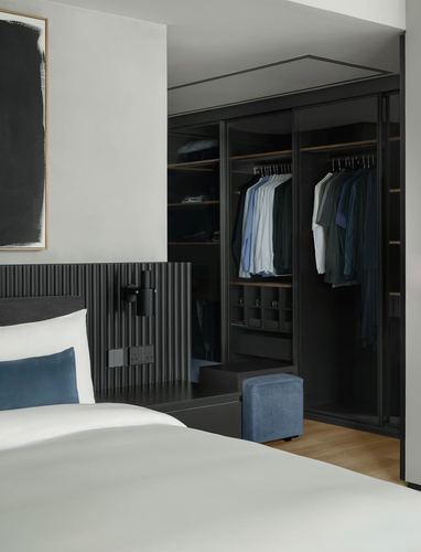 Bedroom with fluted charcoal headboard opening into a walk-in wardrobe with hanging clothes
