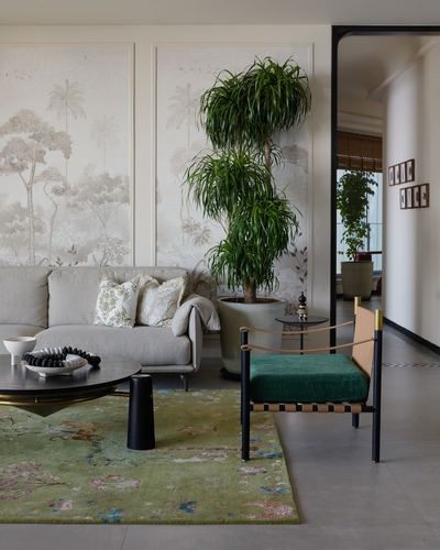 Living room with mural wallpaper, tall potted plant, grey sofa, green rug and cane-leather armchair.