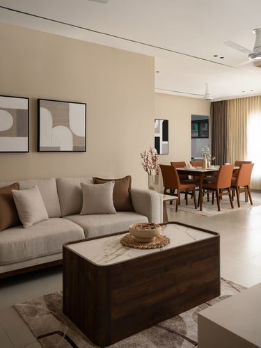 Beige living room with grey sofa, marble-top wood coffee table, and dining area visible beyond