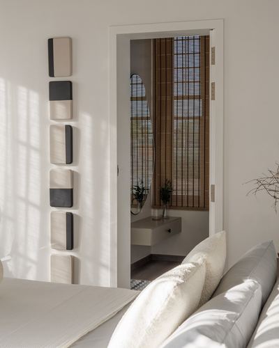 Sunlit bedroom corner with stacked wall tiles beside doorway revealing console and oval mirror