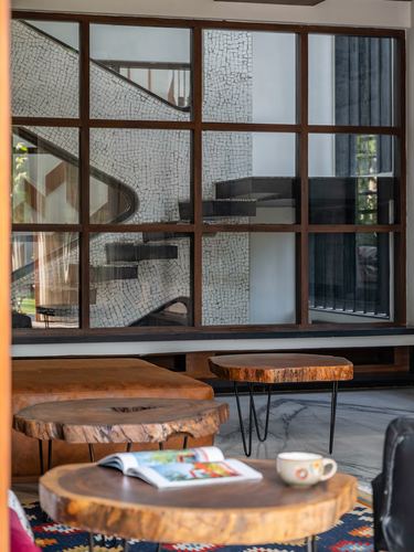 Live-edge wooden coffee tables in front of a large steel-framed window showing a mosaic staircase beyond