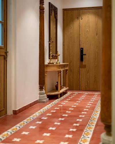 Foyer with turned wooden pillar, carved mirror console, and red patterned tile floor leading to wooden door