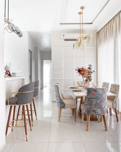 Dining room with floral upholstered chairs, marble-topped table, and brass chandelier against paneled wall
