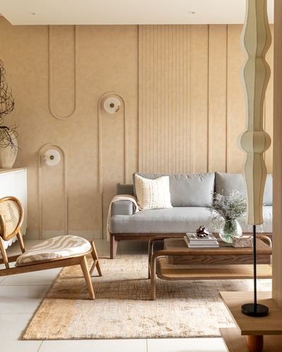 Warm-toned living room with grey sofa, cane chair, and sculptural wall niches with lamps