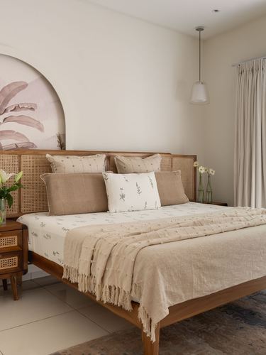 Bed with cane headboard against arched pink mural, layered neutral linens, pendant light beside curtained window