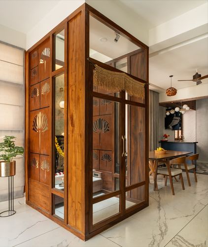 Carved wood and glass pooja enclosure with macrame fringe beside open dining area