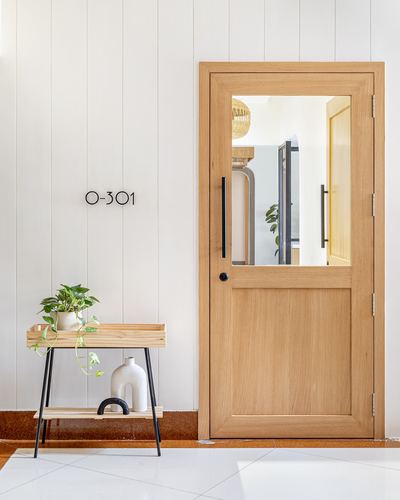Wood-paneled entry door with glass pane beside a small console table with plants, unit O-301