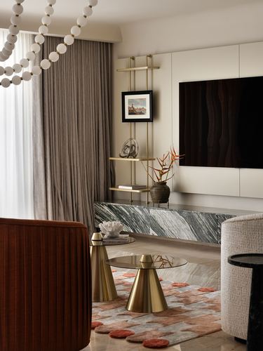 Living room corner with stone tv console, brass etagere, velvet chair and beaded chandelier