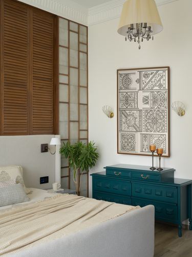 Bedroom with louvered wood partition, framed decorative panel art, and teal chest of drawers