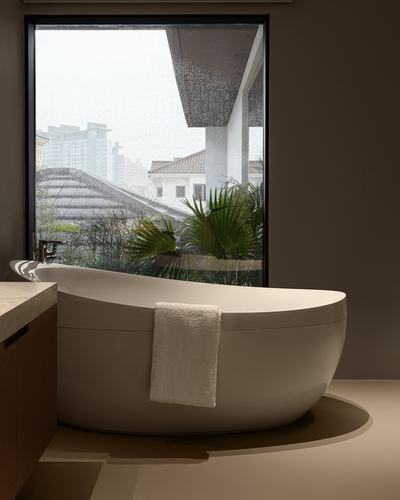 Sculptural freestanding tub before large window overlooking Dubai rooftops and palms