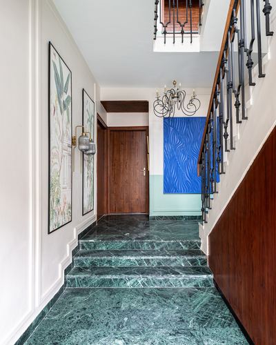 Entry hallway with green marble steps leading to a wooden staircase with iron balustrade and framed art