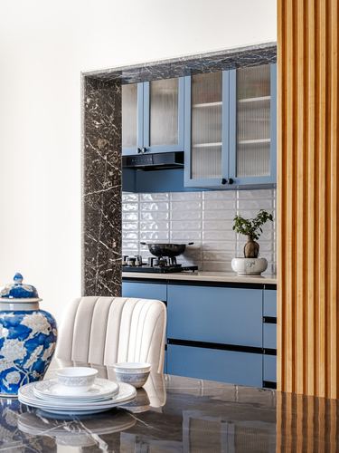 Blue cabinetry kitchen niche framed in dark marble, dining table with blue-white china in foreground
