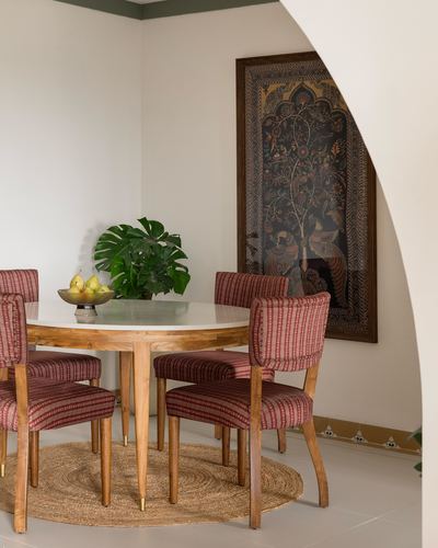 Round dining table with striped chairs beneath framed kalamkari textile, seen through a curved archway