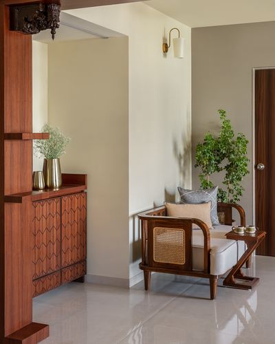 Foyer nook with carved wood sideboard, cane armchair, brass sconce and potted plant