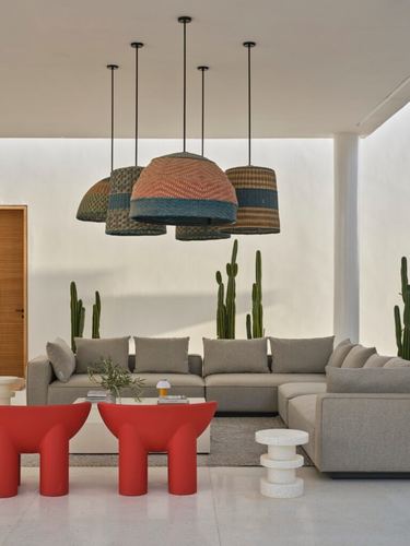 Living area with woven pendant cluster, grey sectional, and red curved armchairs against desert planting