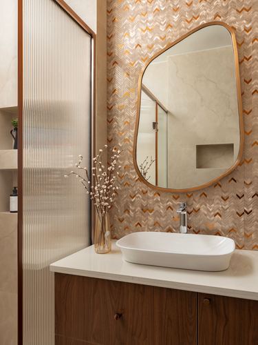Bathroom vanity with organic brass-framed mirror on chevron tile wall above vessel sink and wood cabinetry