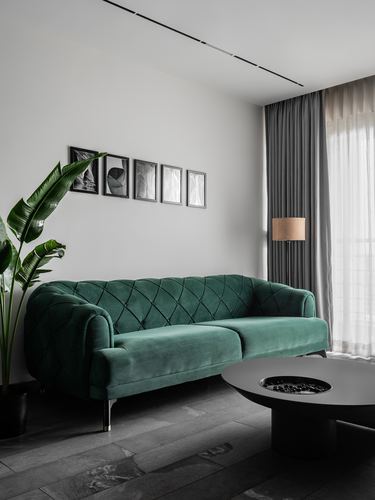 Green tufted sofa against grey stone floor with framed gallery wall and sheer curtains