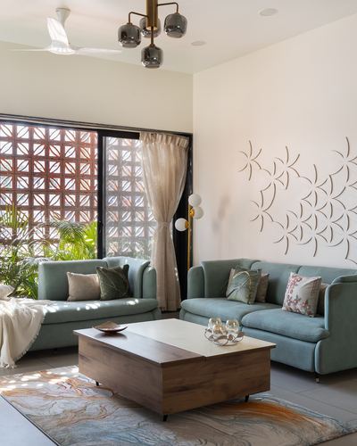 Living room with sage sofas, wooden coffee table, and terracotta jaali window screen