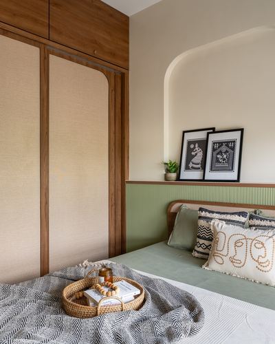 Bedroom corner with wooden wardrobe, arched niche shelf with framed art, and sage green headboard bed