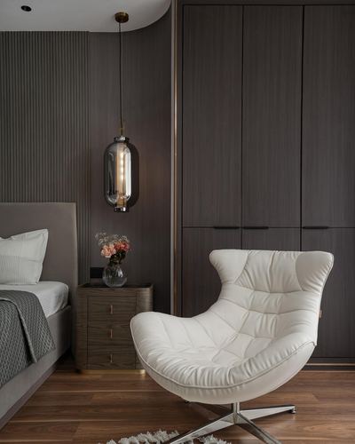 White curved leather lounge chair beside dark wood wardrobe and bedside table with pendant light