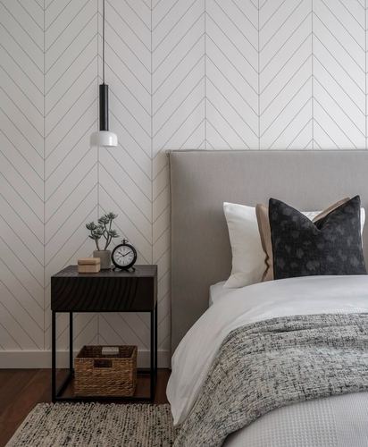 Grey upholstered bed with black pillow beside dark wood nightstand against a chevron wall panel