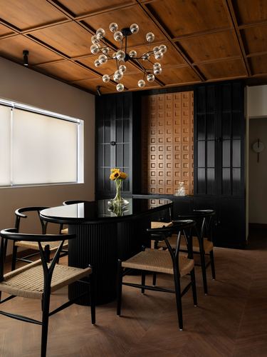 Dining room with oval black table, wishbone chairs, sputnik chandelier, and coffered wood ceiling