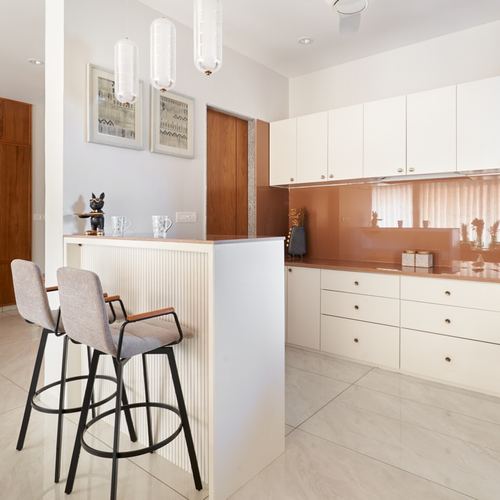 White kitchen with terracotta glass backsplash, marble breakfast counter, and grey bar stools