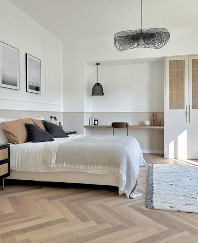 Neutral bedroom with herringbone wood floor, woven black pendant, cane wardrobe, and layered bedding