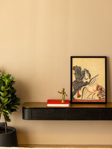 Floating black console with framed Indian miniature painting, brass figurine, and plant against beige wall