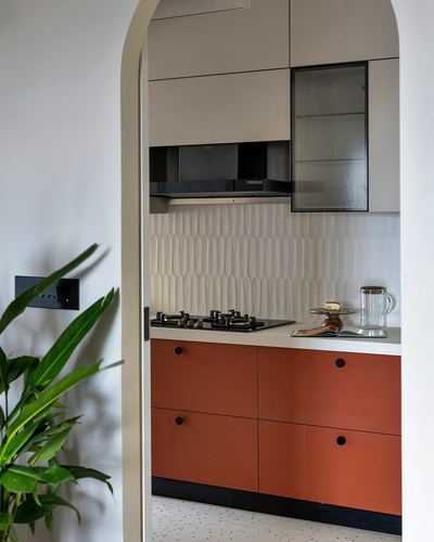 Terracotta lower cabinets and beige upper units in a kitchen framed by an arched doorway