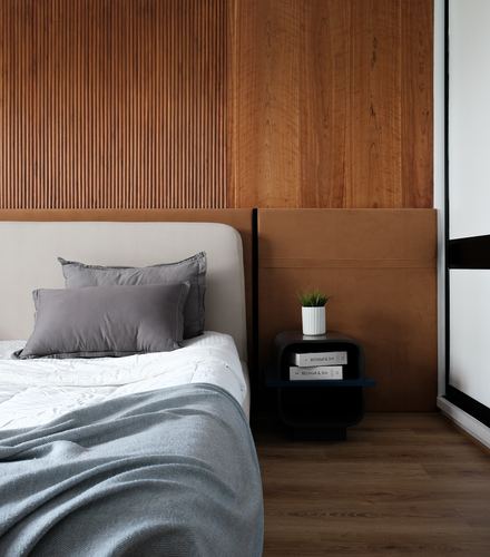 Bedroom corner with fluted wood wall, leather headboard, and round black nightstand