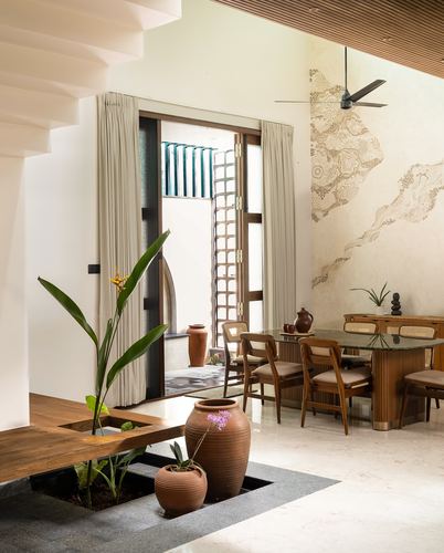 Dining area with cane chairs, terracotta pots, and sunken planter beside a stone floor