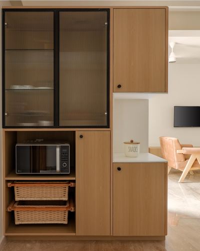 Wood kitchen cabinetry with fluted glass shutters, microwave niche, and cane baskets, living room beyond