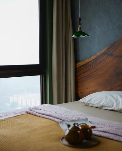 Bed with live-edge wood headboard, green pendant lamp, and tea tray beside window